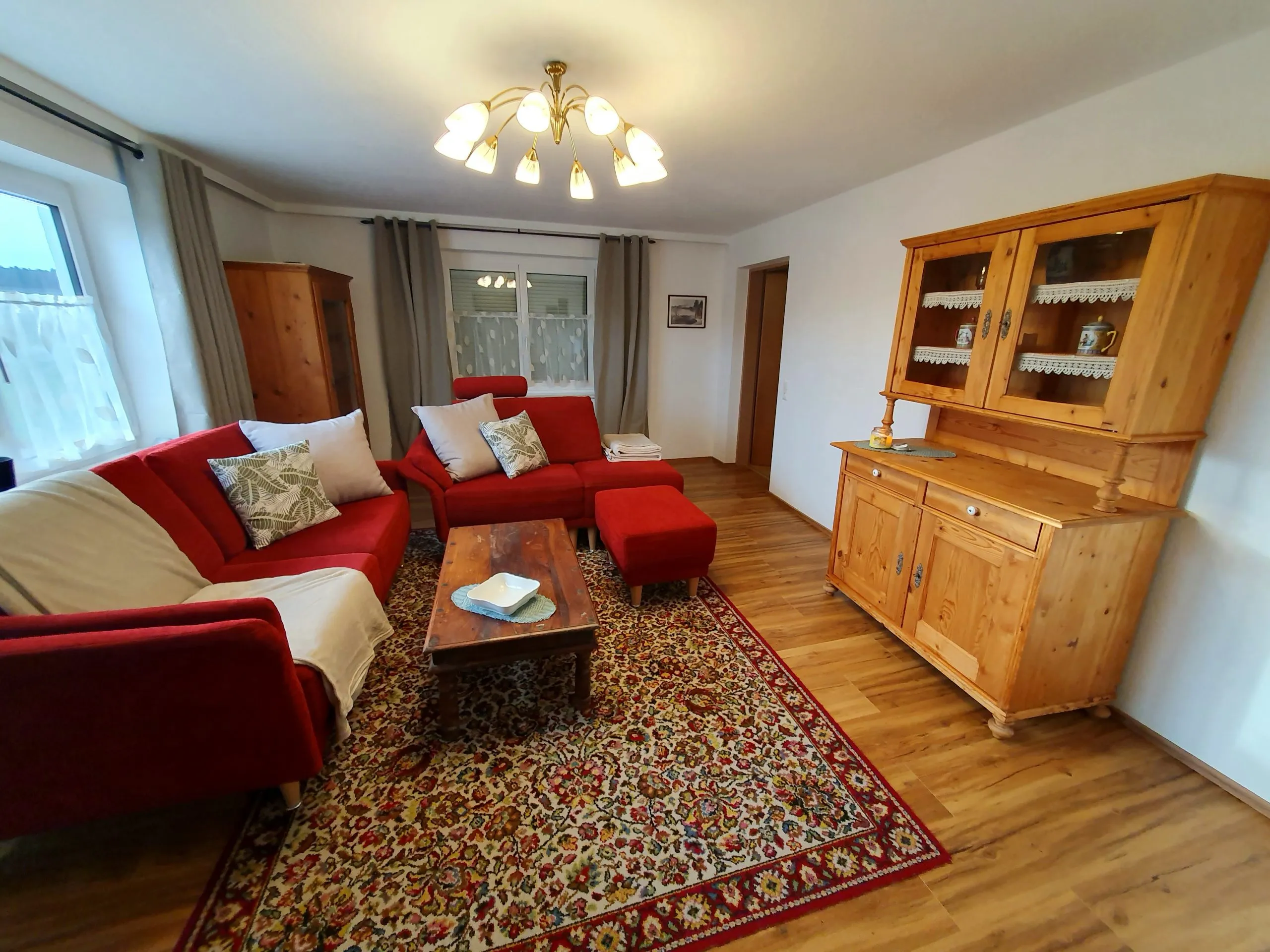 Wohnzimmer mit rotem Sofa, Perserteppich und Bauernschrank
