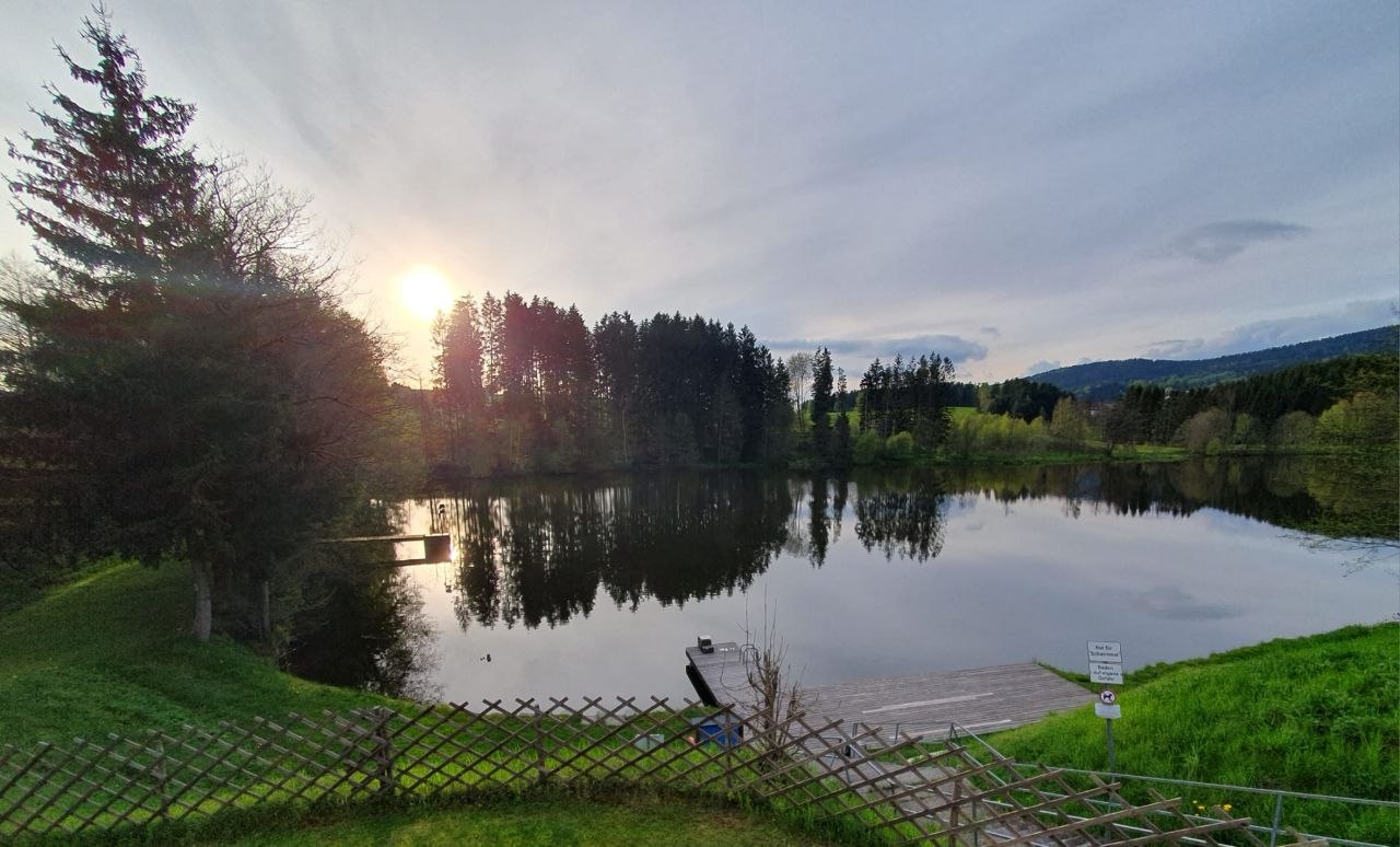 Abendstimmung mit Sonnenuntergang über einem ruhigen See mit Steg am Ufer